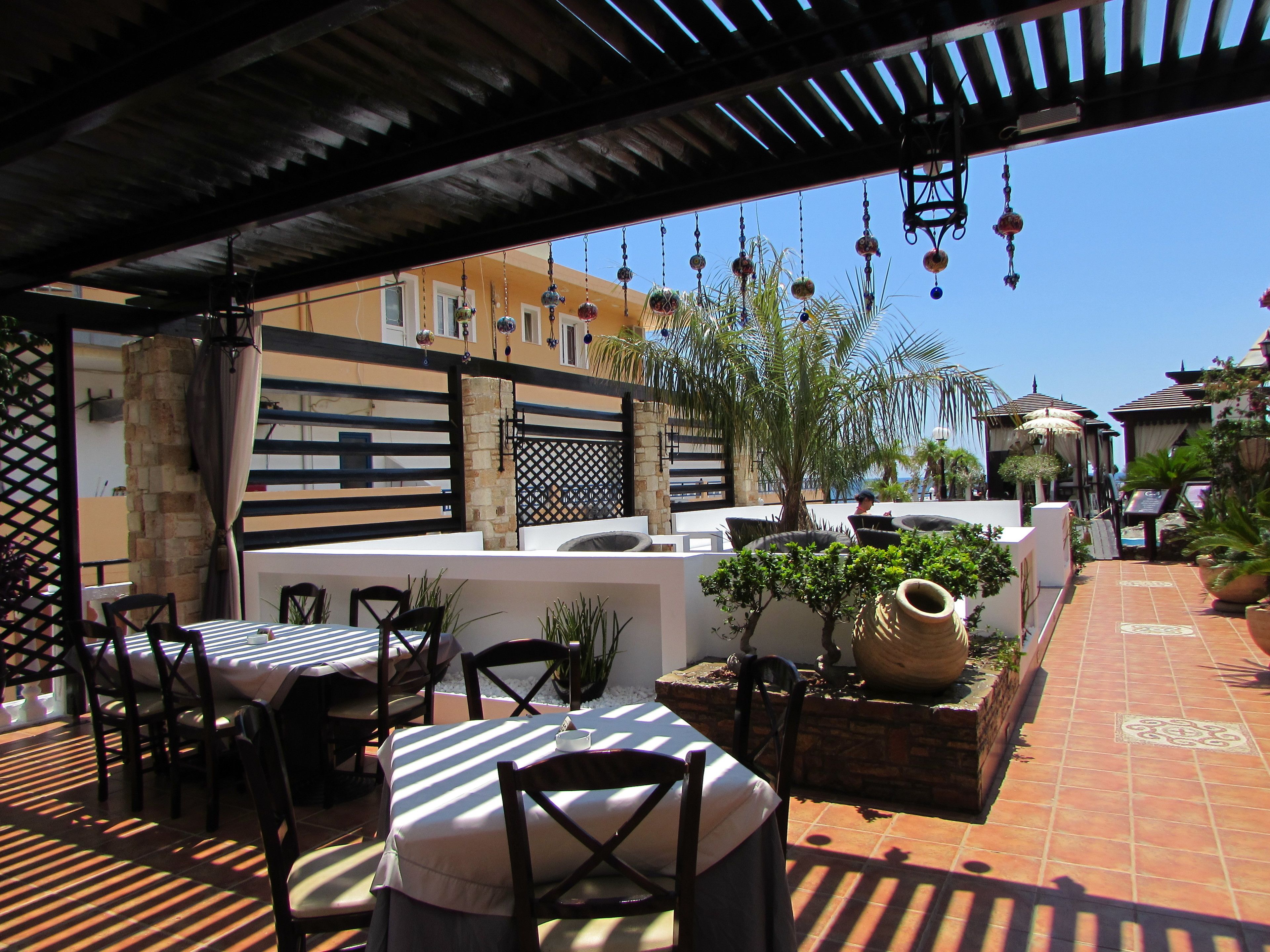 Un espacio de patio al aire libre con mesas y sillas, plantas en macetas y decoración colgante.