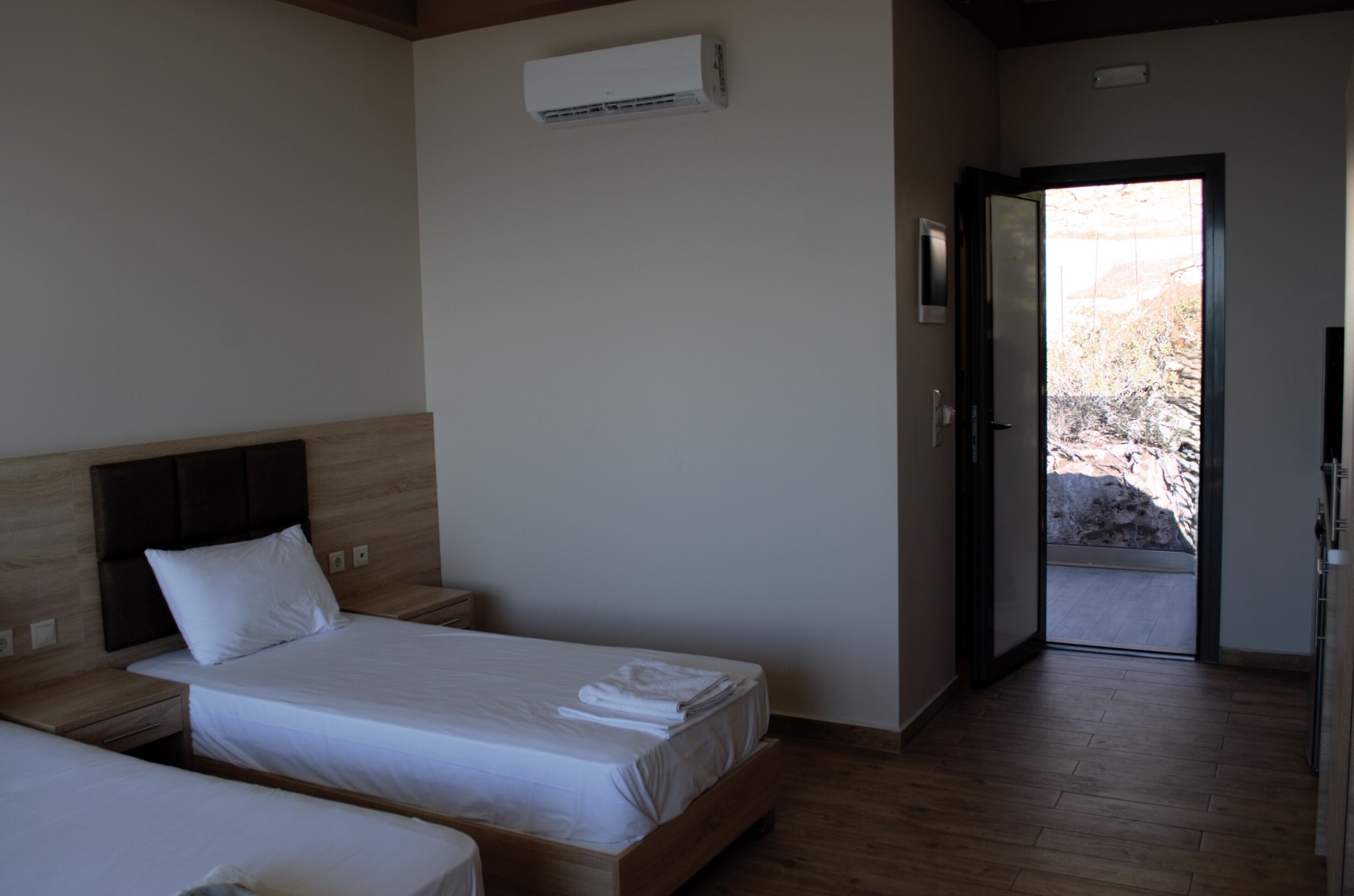 Ein Hotelzimmer mit zwei Betten, Holz-Kopfteilen, einer weißen Klimaanlage und einer Tür zu einem Außenbereich.