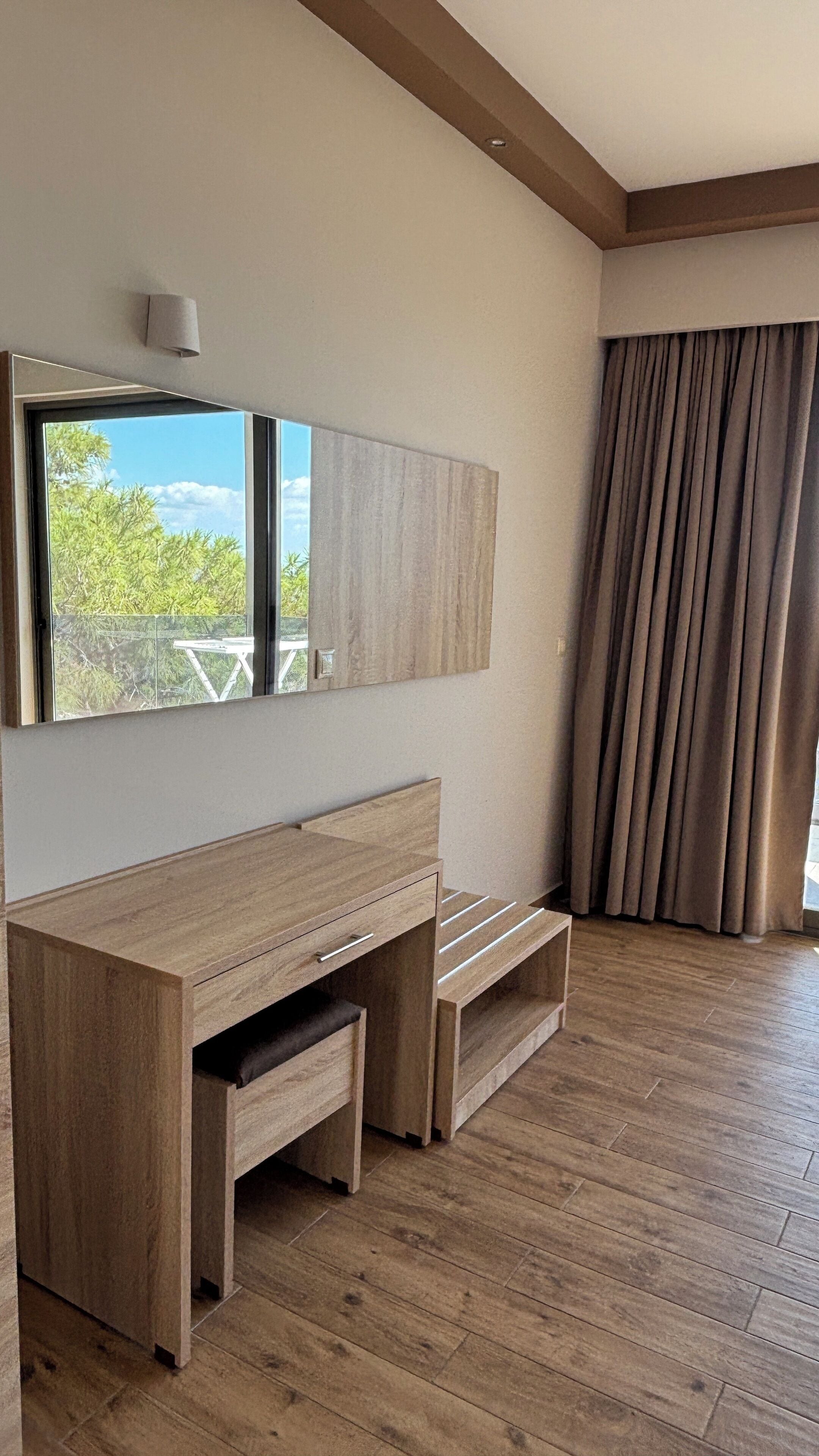 Una habitación moderna con un escritorio de madera, un espejo grande y vistas a zonas verdes.