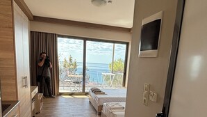 A modern hotel room with a wooden floor, a bed, a desk, and a view of the sea. - Coralli Apartments (Rhodes)