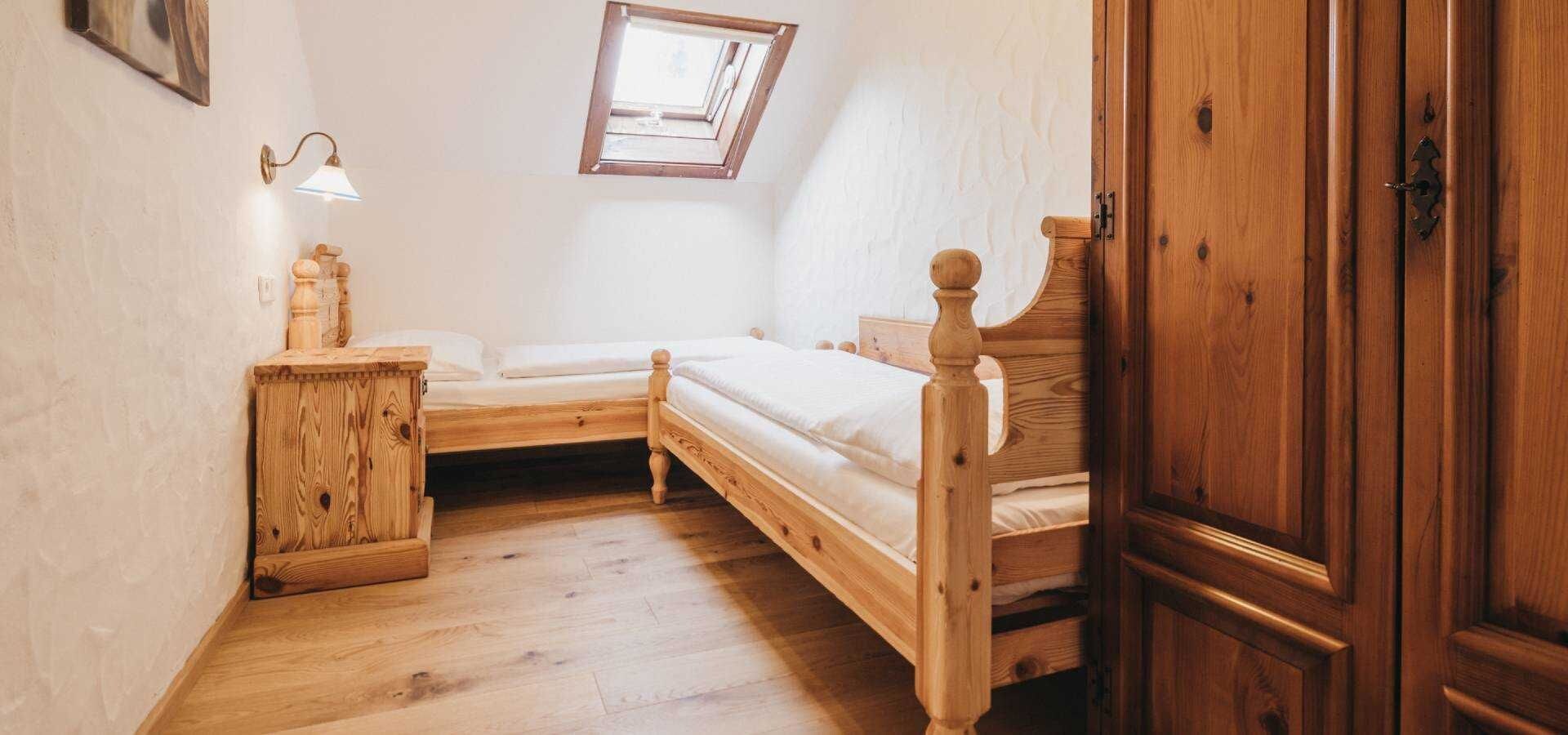 A small, cozy bedroom with two wooden beds, a nightstand, a wooden wardrobe, and a skylight.