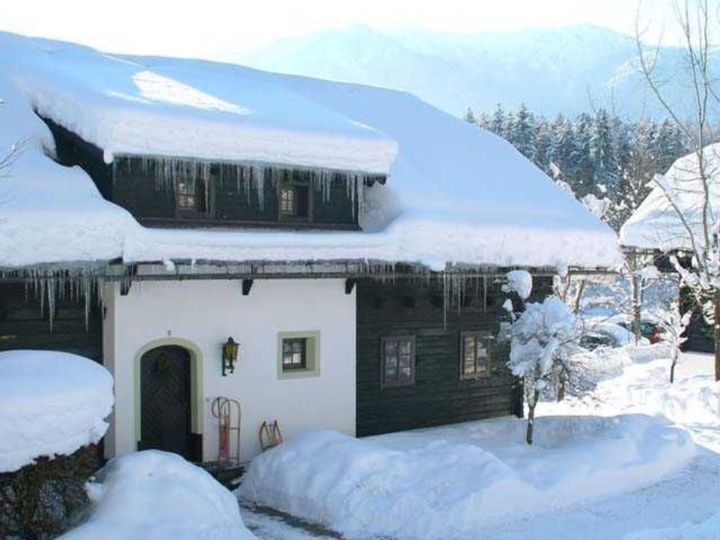 A snow-covered house with a dark exterior, a visible door, and icicles hanging from the roof.