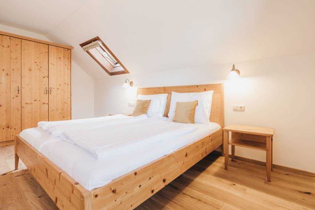 Ein hölzernes Bett in einem Zimmer mit Dachfenster, ein Holzschrank und ein Nachttisch.
