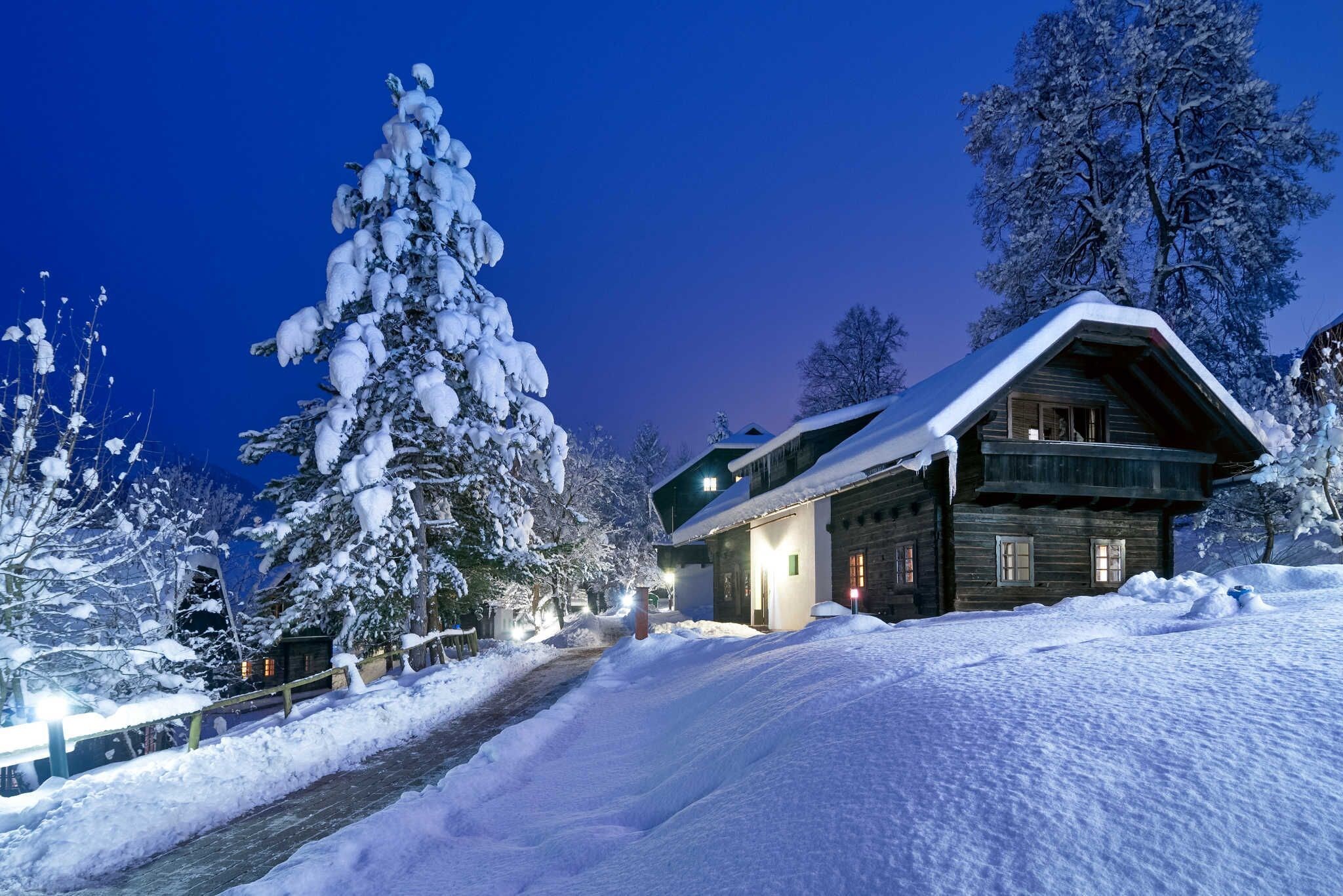 Ein mit Schnee bedecktes Chalet mit Holzfassade, einem gut erkennbaren Eingang und einer verschneiten Auffahrt.