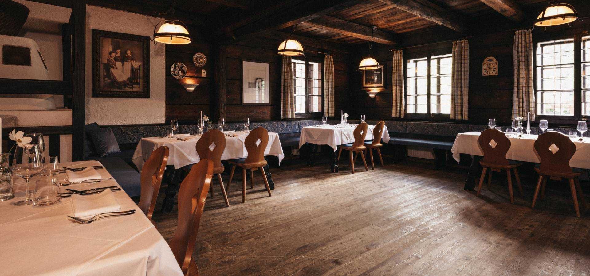 A restaurant with wooden floors, tables set with white tablecloths, and wooden chairs.