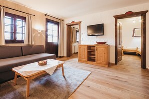 Una sala de estar con sofá, una mesa de madera, televisor y una zona de cocina con armarios.