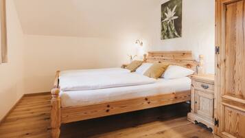 A wooden bed with white bedding, a nightstand with a lamp, and a wooden wardrobe.