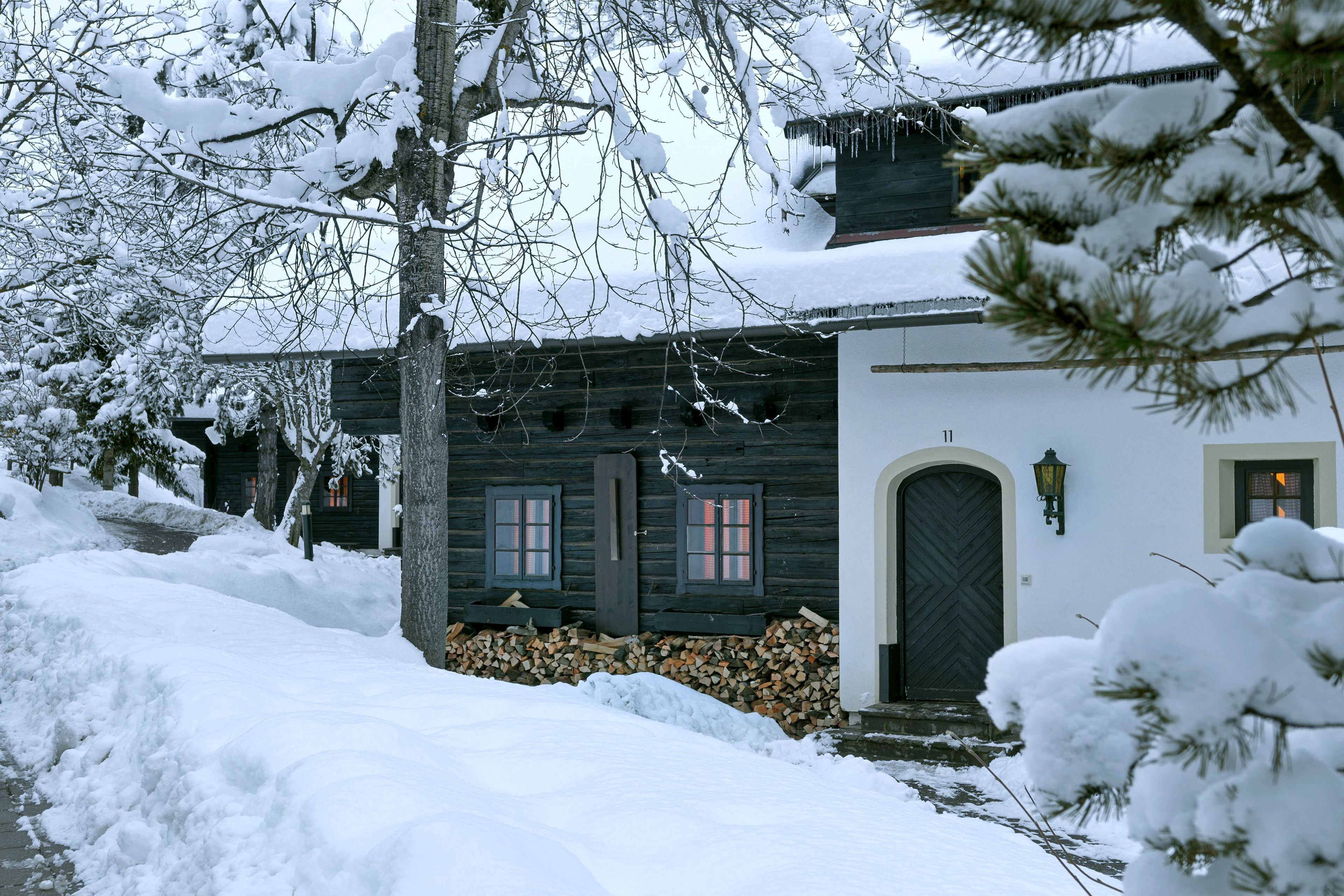 Una casa di legno ricoperta di neve, con una porta e finestre scure, un piccolo portico e un camino ben visibile.