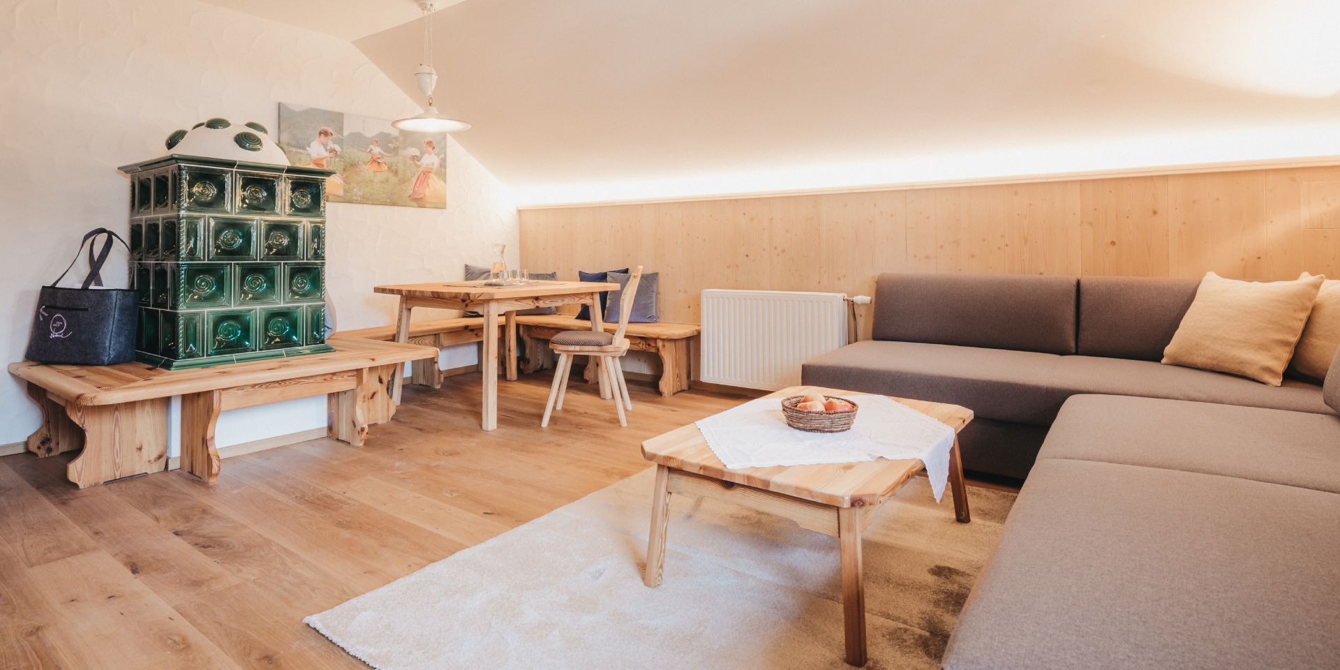 A cozy living room with a wooden bench, a dining table, a sofa, and a radiator.