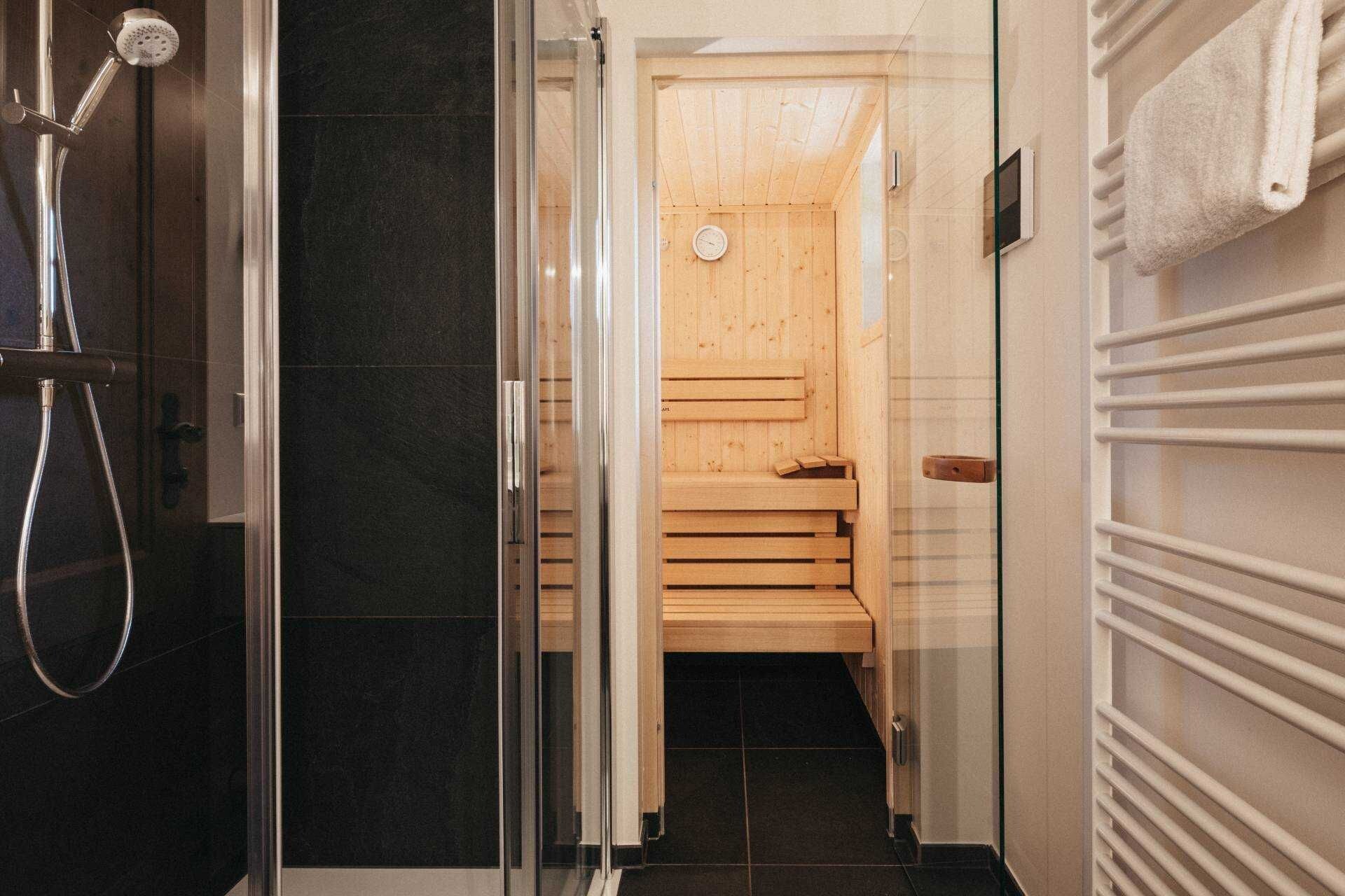 Un baño moderno con cabina de ducha de vidrio, banco de sauna de madera y toallero blanco.