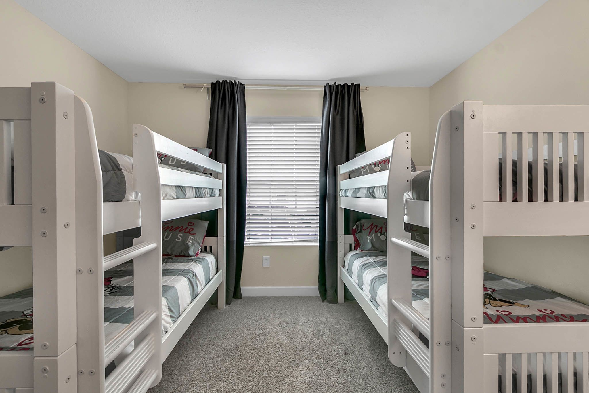 Une chambre avec des lits superposés, une fenêtre avec des stores et un sol recouvert de moquette.