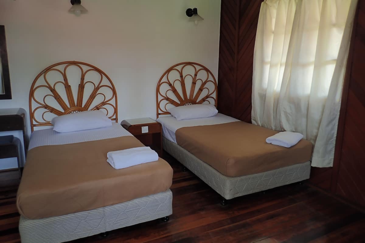 Two single beds with wicker frames and brown bedding, a wooden floor, and a window with curtains.