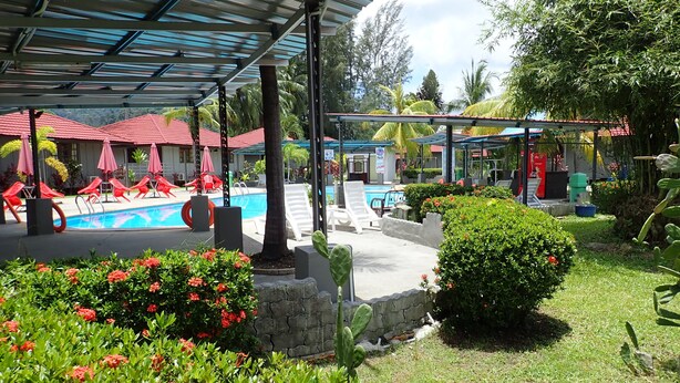 A pool area with lounge chairs, a covered seating area, and a garden with red flowers. - Lemonia Holiday Resort (Langkawi)