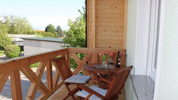 A wooden deck with a round table and chairs, a small potted plant, and a bottle of wine. - Ferienwohnungen Dobra (Lübbenau/Spreewald)