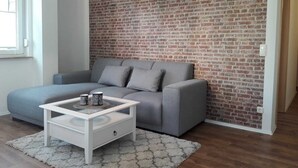 A modern living room with a grey sofa, a white coffee table, and a brick-patterned wall. - Ferienwohnungen Dobra (Lübbenau/Spreewald)