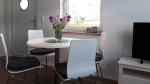 A dining area with a round table, white chairs, a vase with flowers, a hanging lamp, and a TV on a stand. - Ferienwohnungen Dobra (Lübbenau/Spreewald)