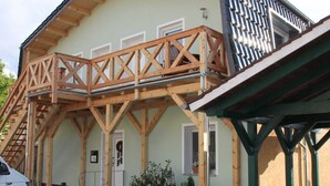 A building with a wooden deck, a covered entrance, and a staircase leading to an upper level. - Ferienwohnungen Dobra (Lübbenau/Spreewald)