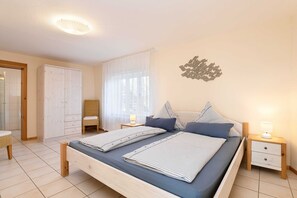 A bedroom with a bed, nightstands, a chair, a wardrobe, and a decorative wall piece.