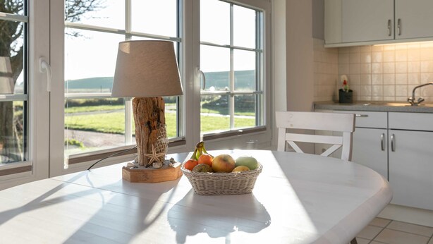 Une cuisine avec une grande fenêtre, une table avec une lampe et un panier de fruits.