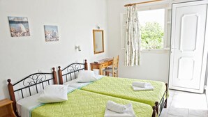 A room with two beds, a wooden desk, a chair, a window with curtains, and a door. - Evagelia's Place (Mykonos)