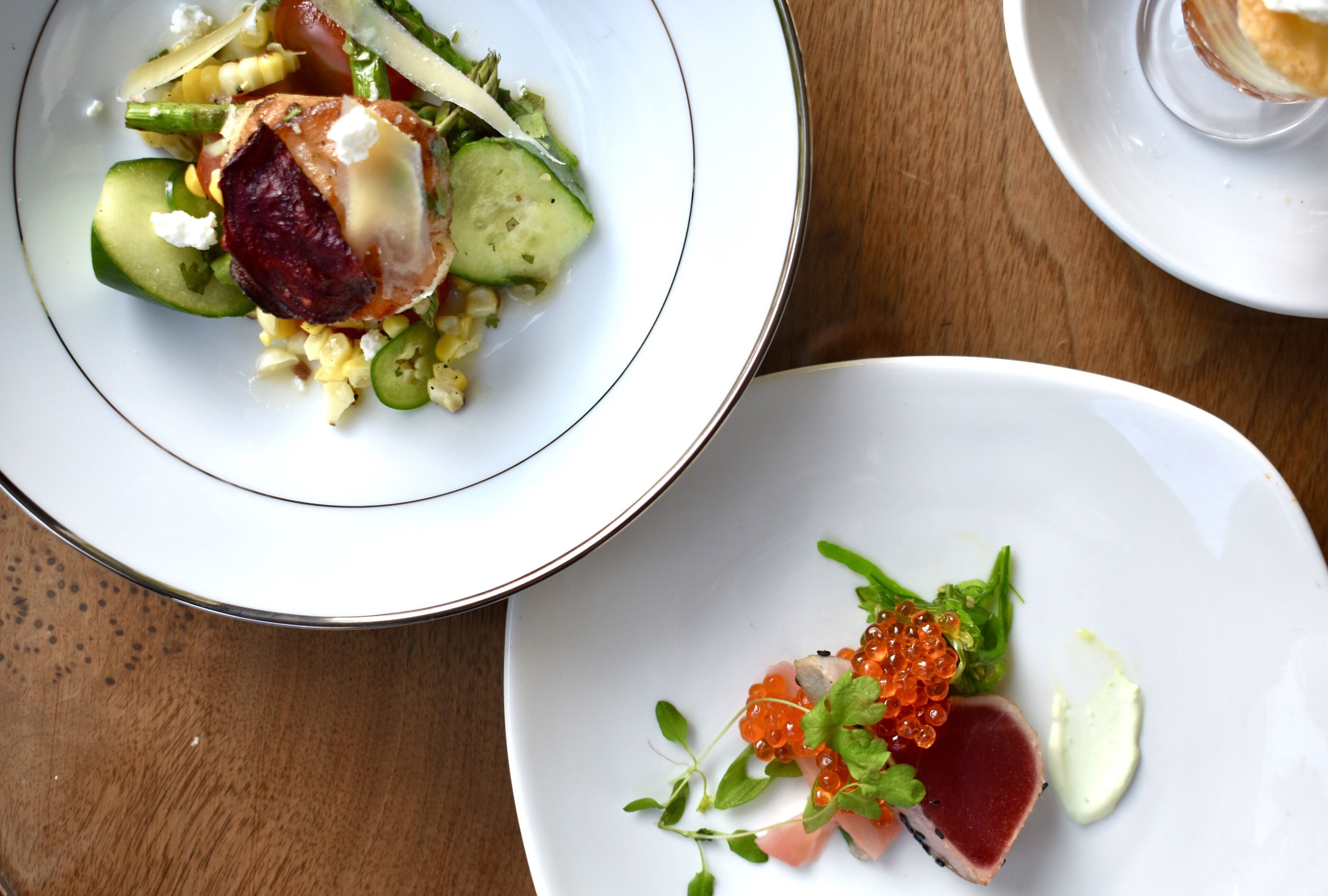 A dining table with two plates of food. One plate has a salad with vegetables and a piece of meat, and the other plate has fish and caviar.