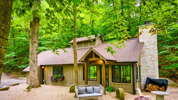 A rustic cabin with a stone chimney, a covered porch, and a seating area with a sofa and a table. - The Morris Estate (Niles)