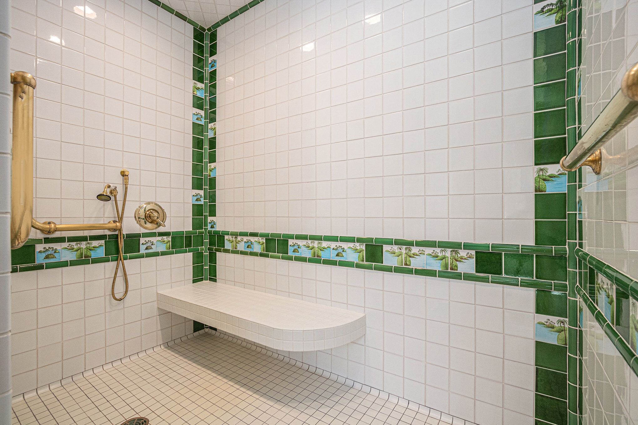 A bathroom with white tiles, a green-tiled accent wall, a white bathtub, and a gold shower fixture.