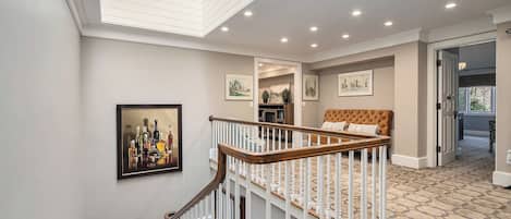 Un hall d’entrée spacieux avec un escalier menant à une chambre. Le hall est doté d’un sol imitant la pierre, d’une œuvre d’art encadrée au mur et d’un plafond pourvu d’un éclairage encastré.