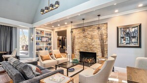 A spacious living room with a fireplace, comfortable seating, a bookshelf, and a modern chandelier. - The Morris Estate (Niles)