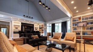 A spacious living room with a black sofa, beige armchairs, and a coffee table. There is a bookshelf filled with books and decorative items. - The Morris Estate (Niles)