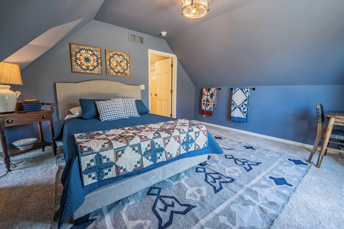 Een slaapkamer met een groot bed, een nachtkastje, een lamp en een deur naar een andere kamer.