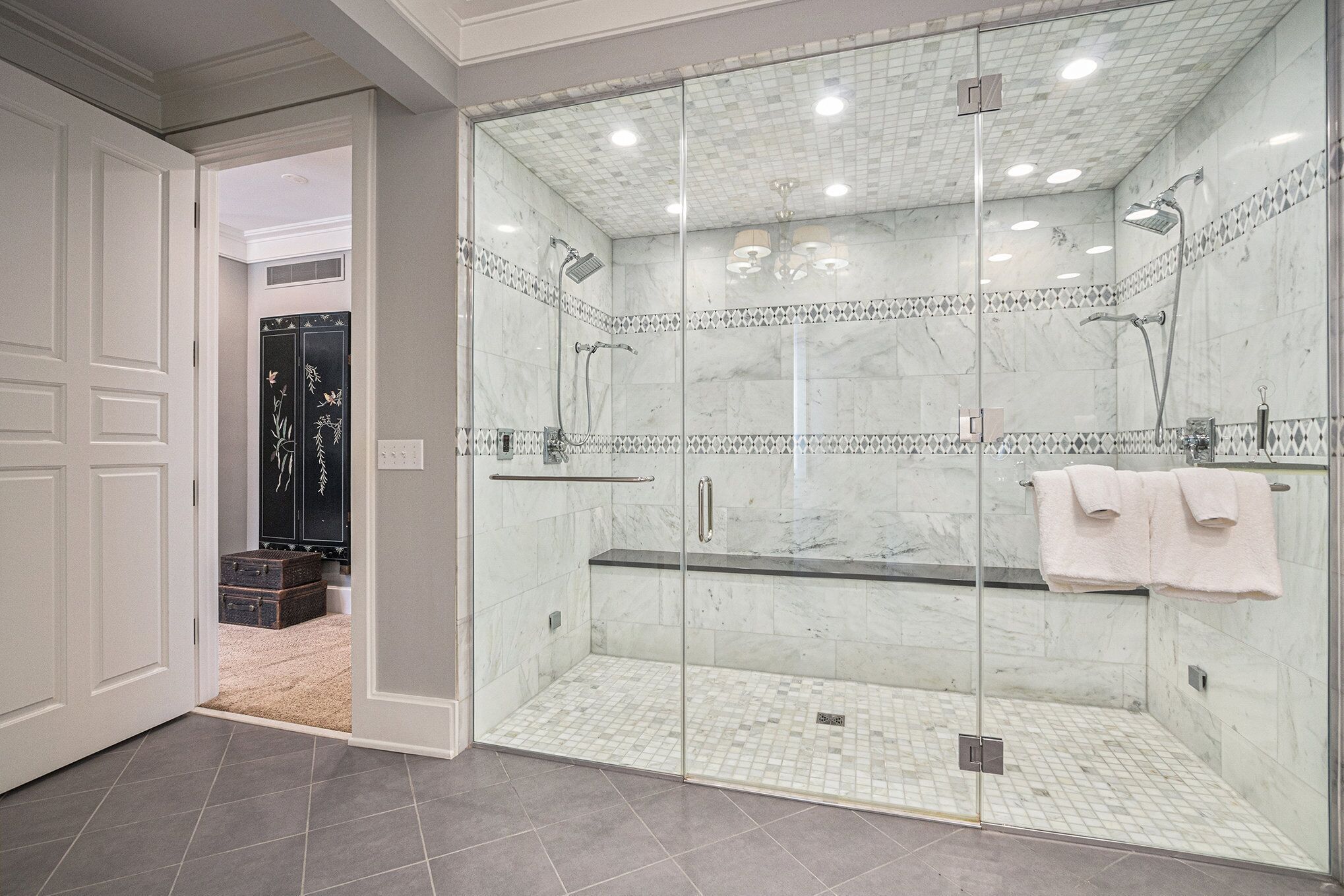 A modern bathroom with a glass-enclosed shower, marble tiles, and a visible towel rack.