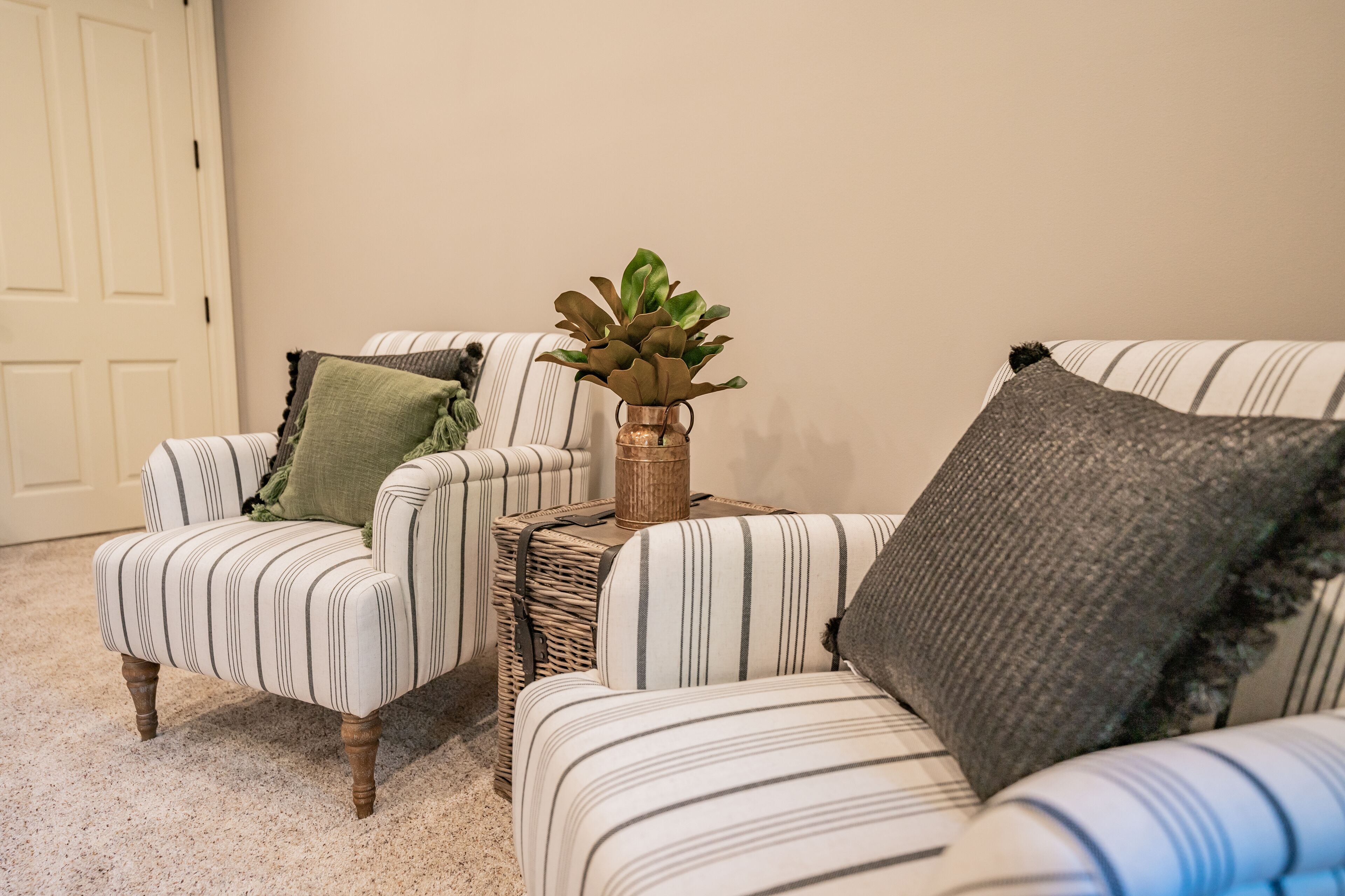 Two striped armchairs with a woven side table and a potted plant between them.