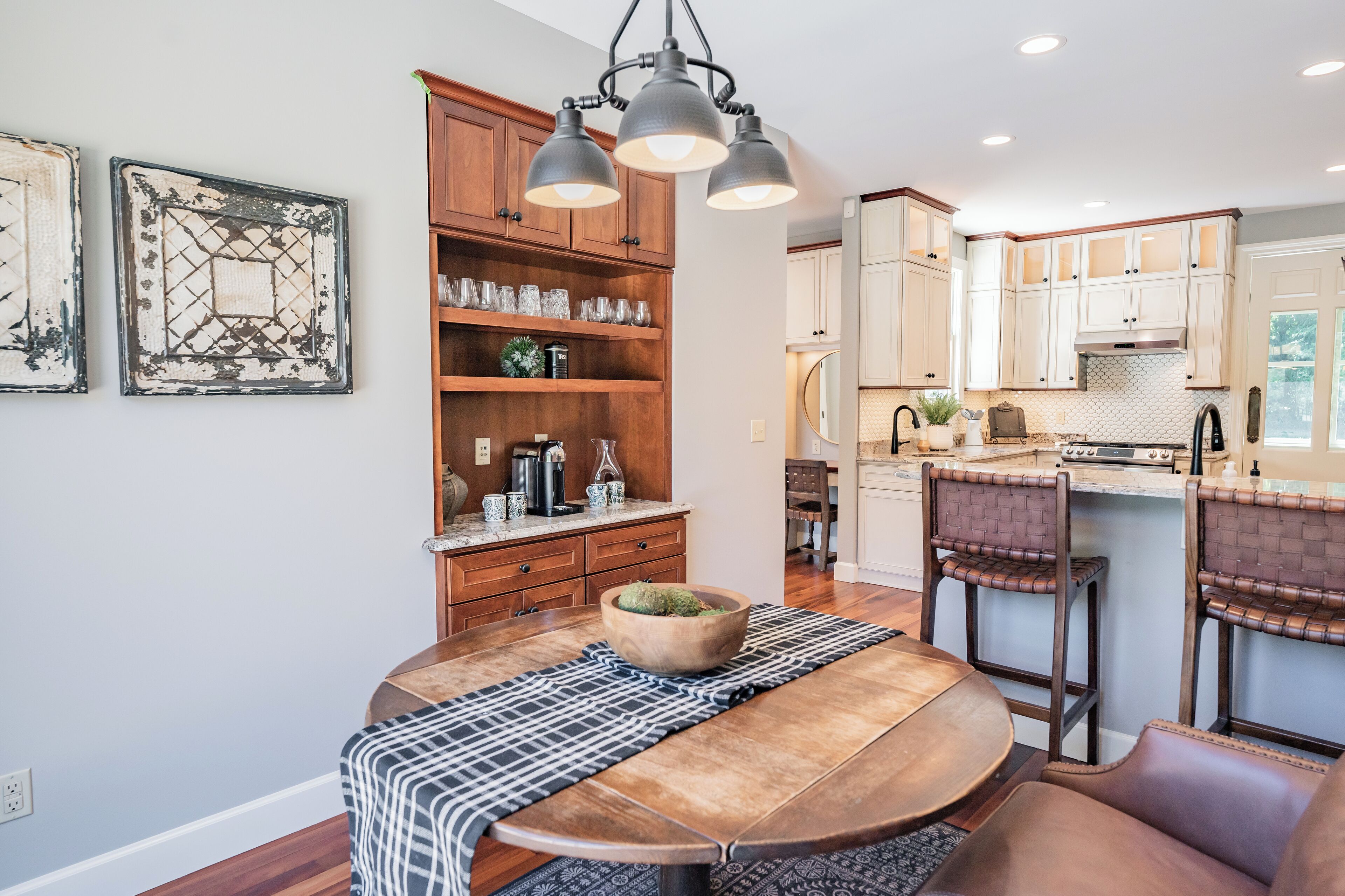 A modern kitchen with wooden cabinets, a dining table with a placemat, and pendant lighting.