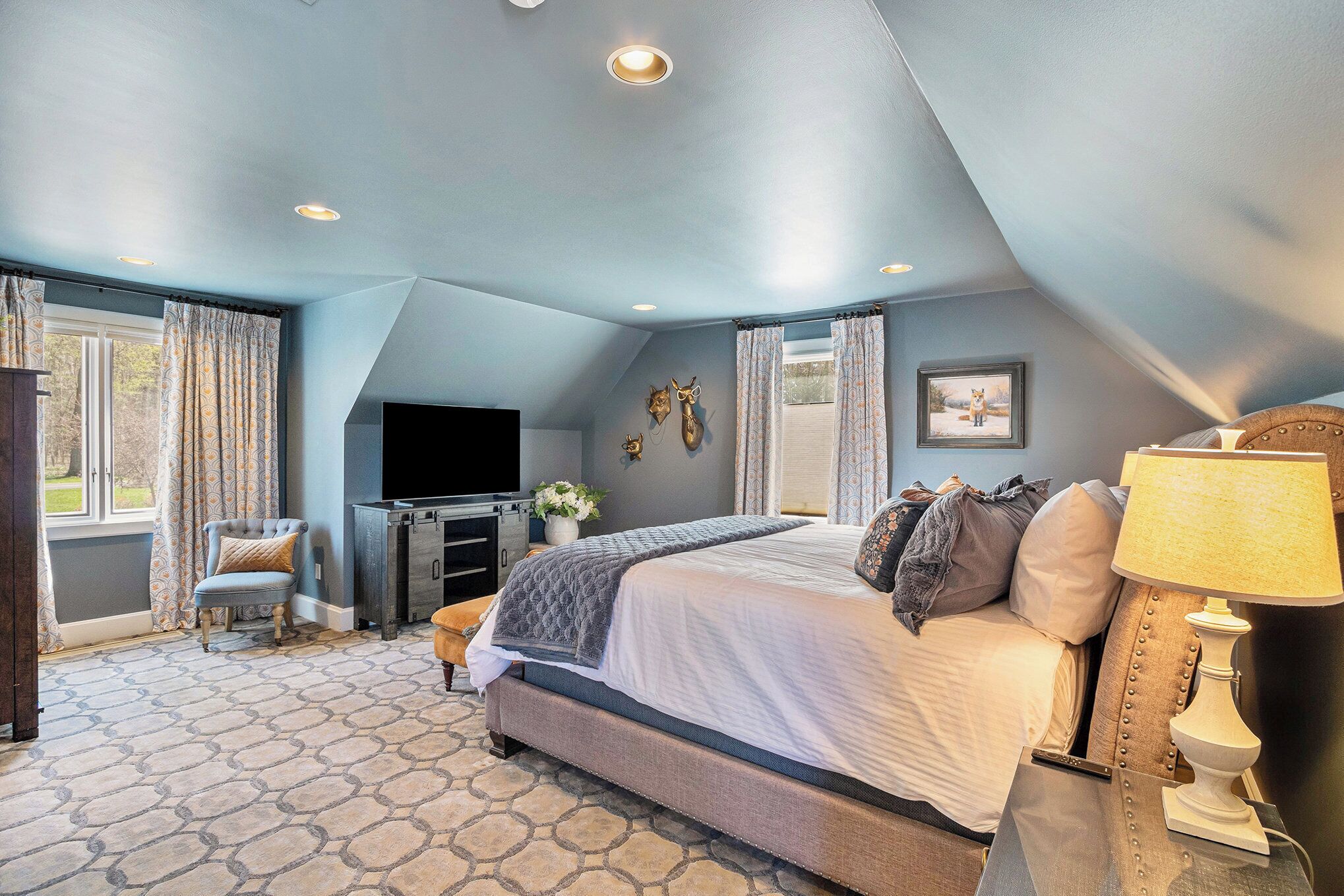 A bedroom with a large bed, a TV, a desk, and a window with curtains.