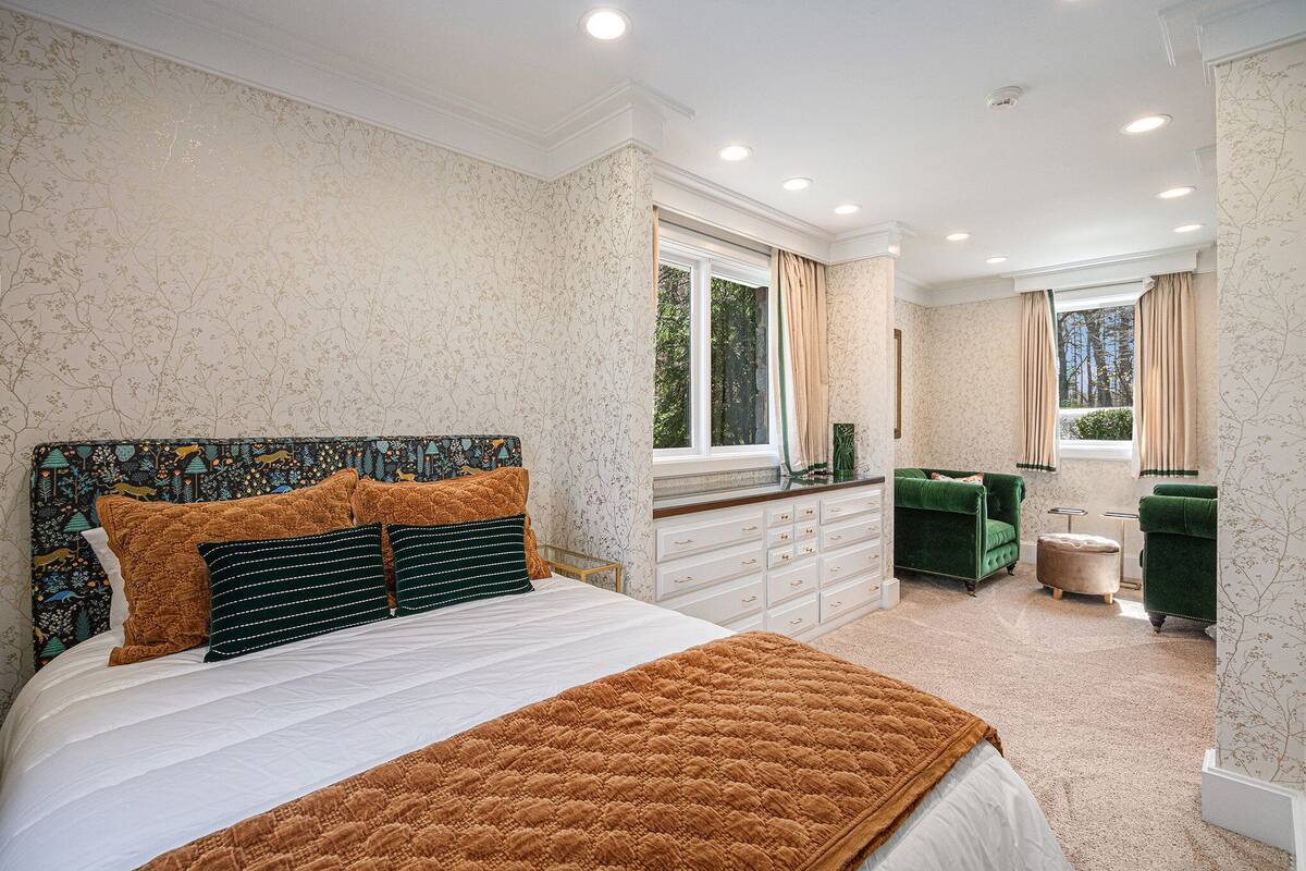 Een slaapkamer met een groot bed, een kaptafel, twee groene fauteuils en een raam met gordijnen.