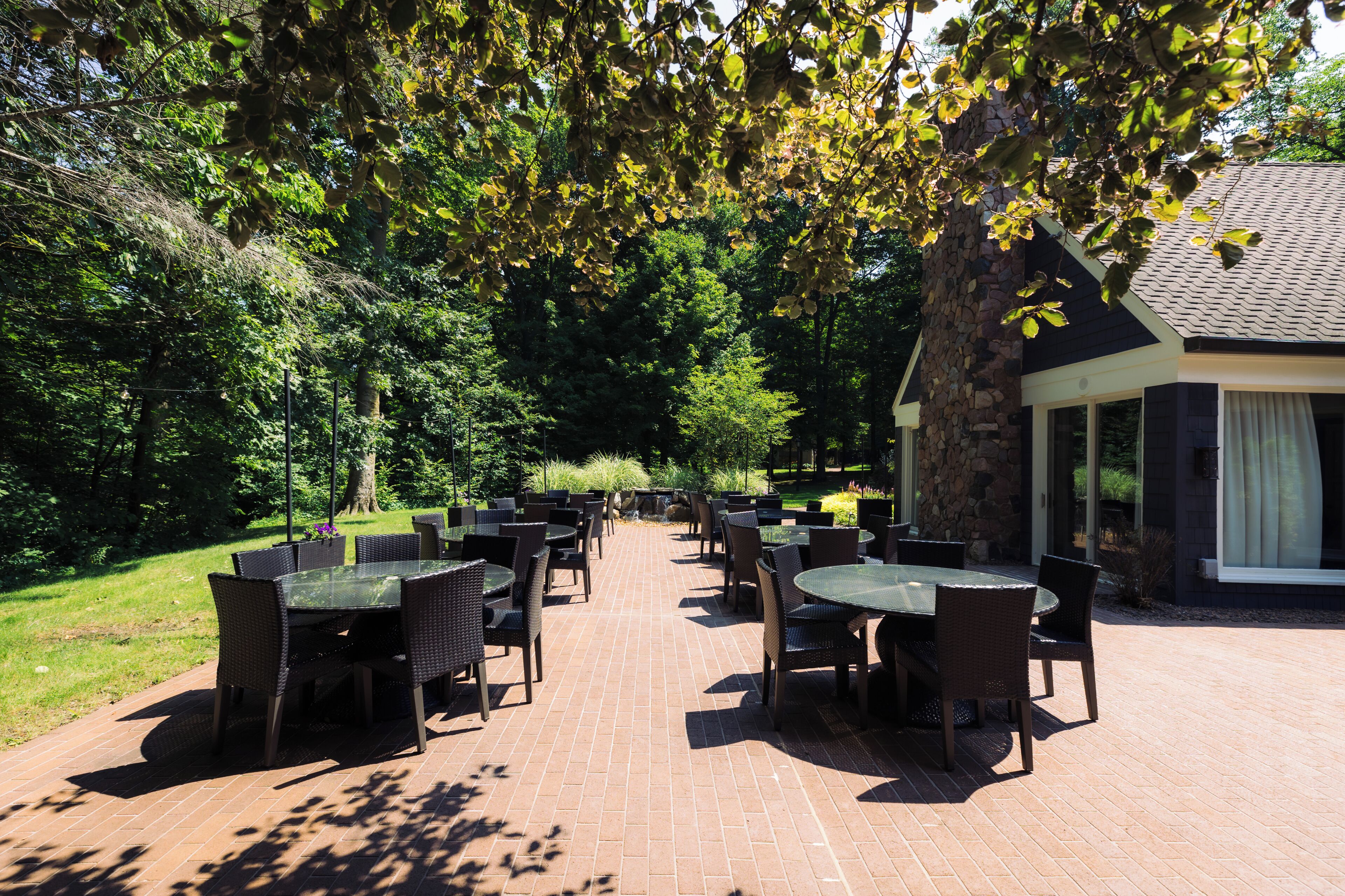 An outdoor patio area with multiple tables and chairs, surrounded by lush greenery and a stone wall.