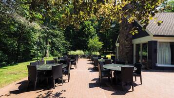 An outdoor patio area with multiple tables and chairs, surrounded by lush greenery and a stone wall.