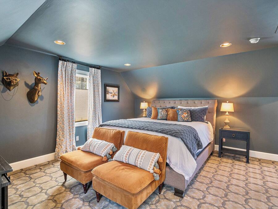 A bedroom with a large bed, two ottomans, a nightstand, and decorative wall art.