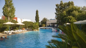 A swimming pool with lounge chairs and umbrellas, surrounded by trees and buildings. - Notos Hotel (Rhodes)