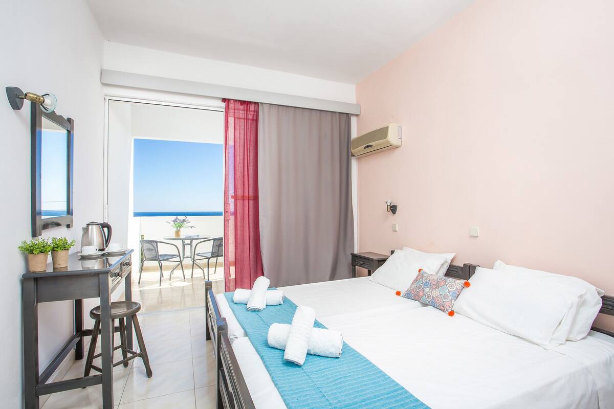 Habitación de hotel con cama, escritorio, silla, mesa y balcón con vistas.