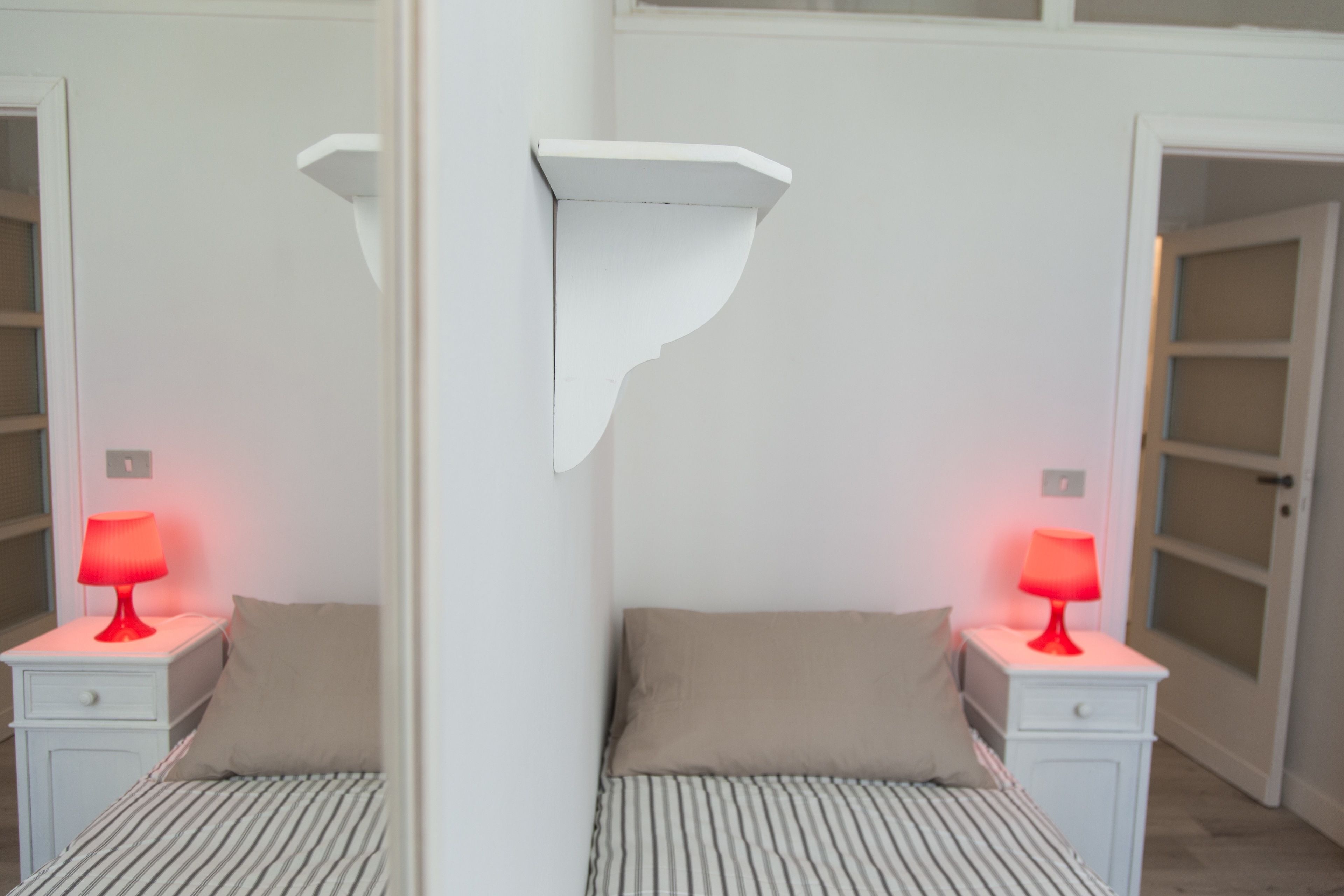 Ein Zimmer mit Spiegel, einem Bett und je einem Nachttisch und einer roten Lampe an jeder Seite.