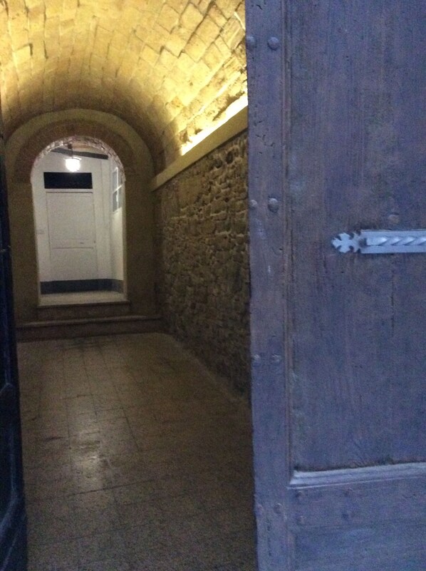 Un pasillo de paredes de piedra con piso de baldosas, que conduce a una puerta con manija metálica.