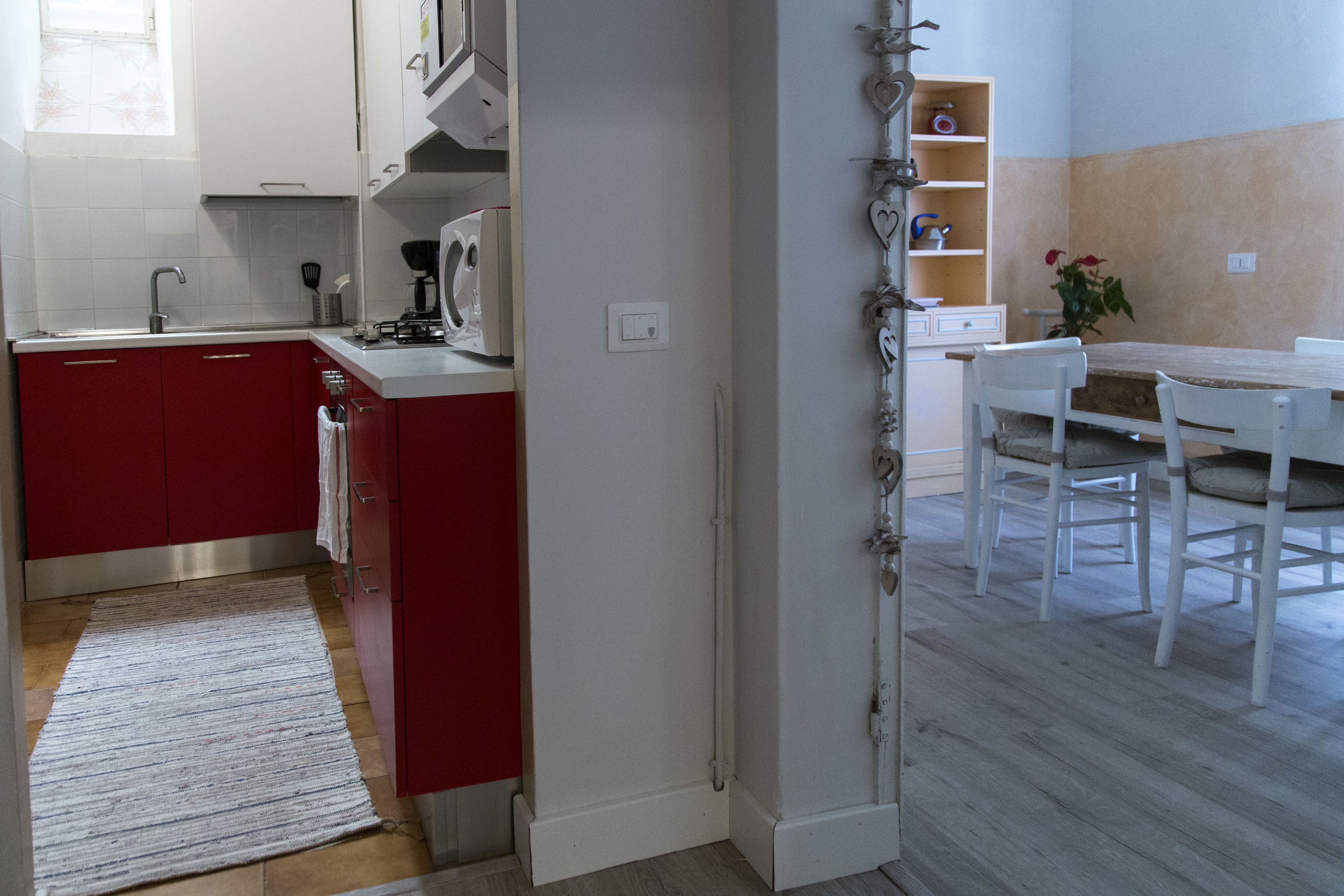 A kitchen with red cabinets, a white countertop, and a dining area with a white table and chairs.
