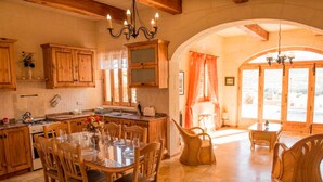 A rustic kitchen with wooden cabinets, a dining table with chairs, and a chandelier. - Country View (Ghasri)