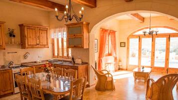 A rustic kitchen with wooden cabinets, a dining table with chairs, and a chandelier.
