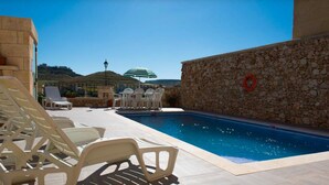 A swimming pool with lounge chairs and umbrellas, surrounded by stone walls and a clear view of the hills. - Country View (Ghasri)