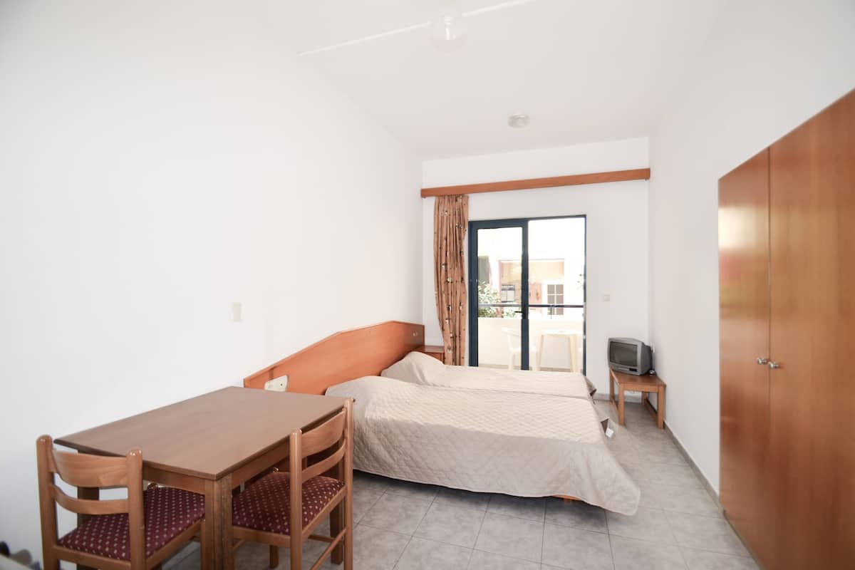 A bedroom with a bed, a wooden desk, a chair, a television on a small table, and a wardrobe.