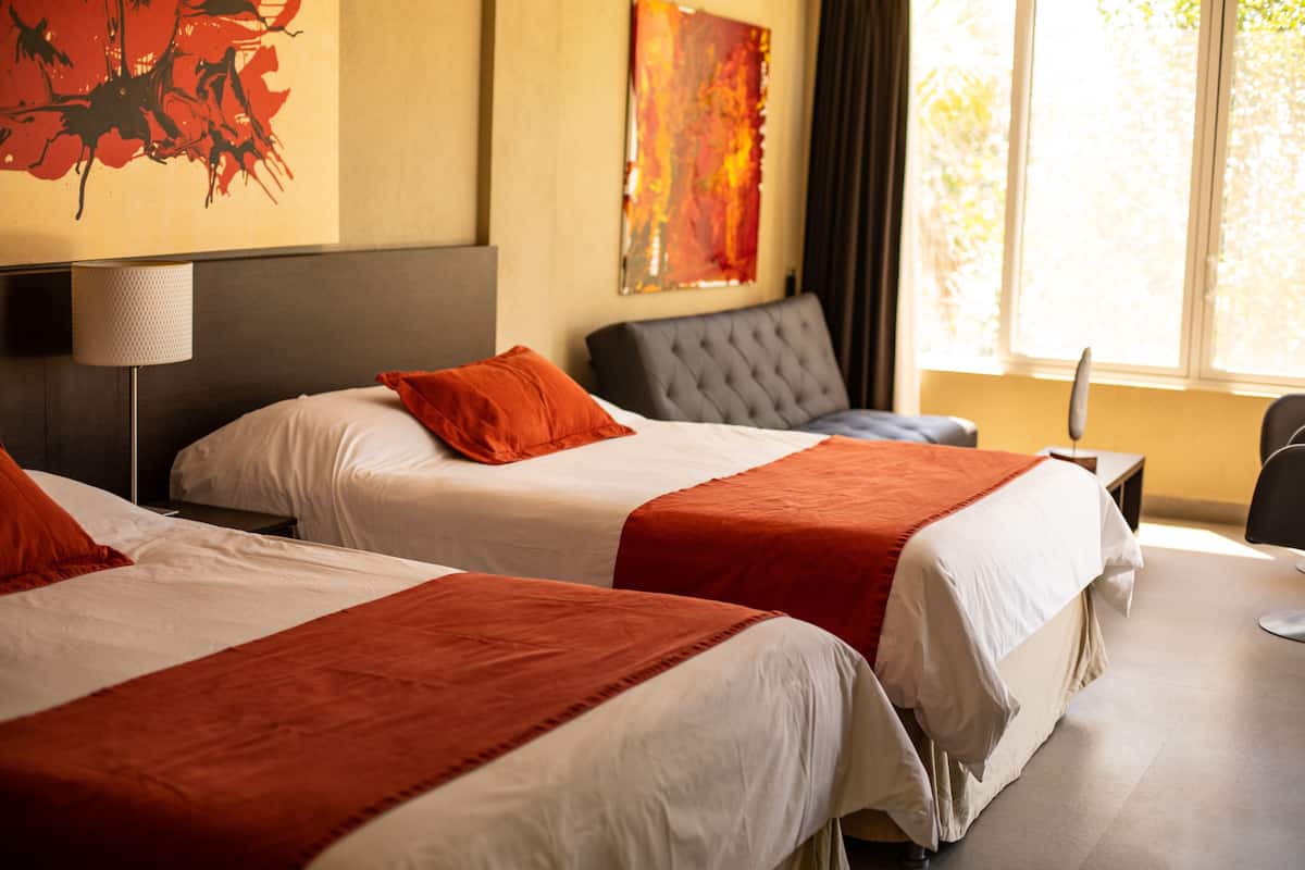 Une chambre d’hôtel avec deux lits, un bureau, une chaise et une fenêtre avec des rideaux.