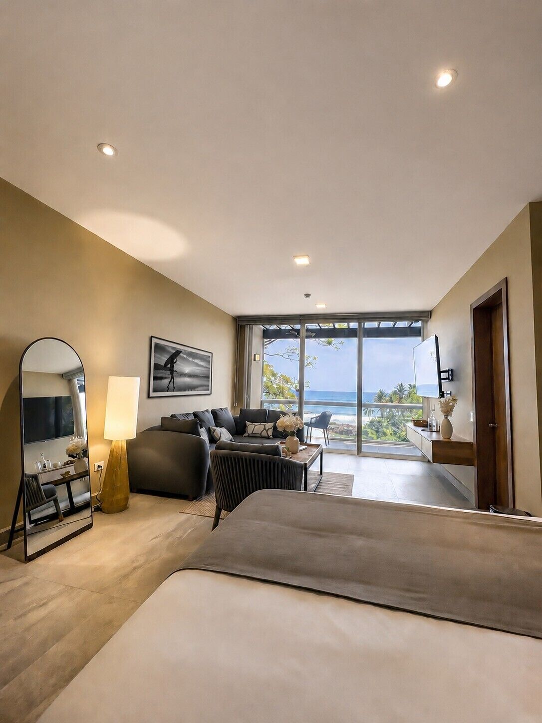 A modern bedroom with a large bed, a sofa, a desk, and a view of the ocean.